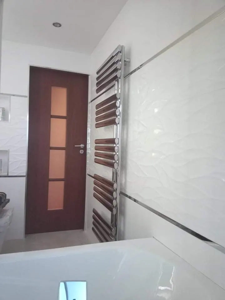 Bathroom with white wave-textured tiles, a chrome towel radiator and a timber door