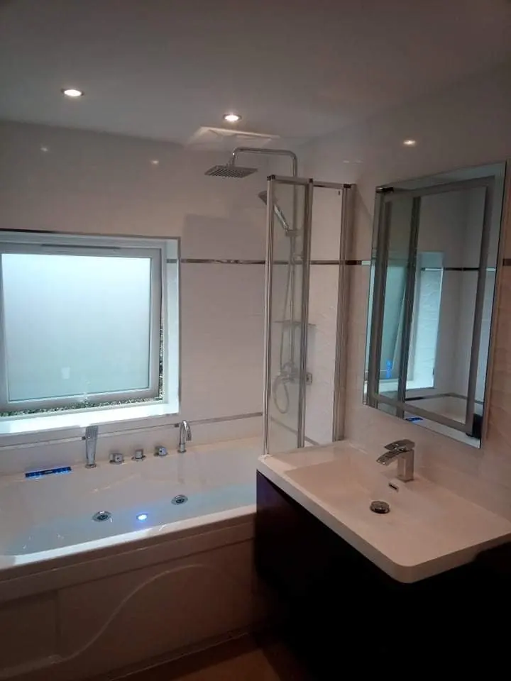 Bathroom with a whirlpool bath, wall-hung vanity, illuminated mirror and rain shower