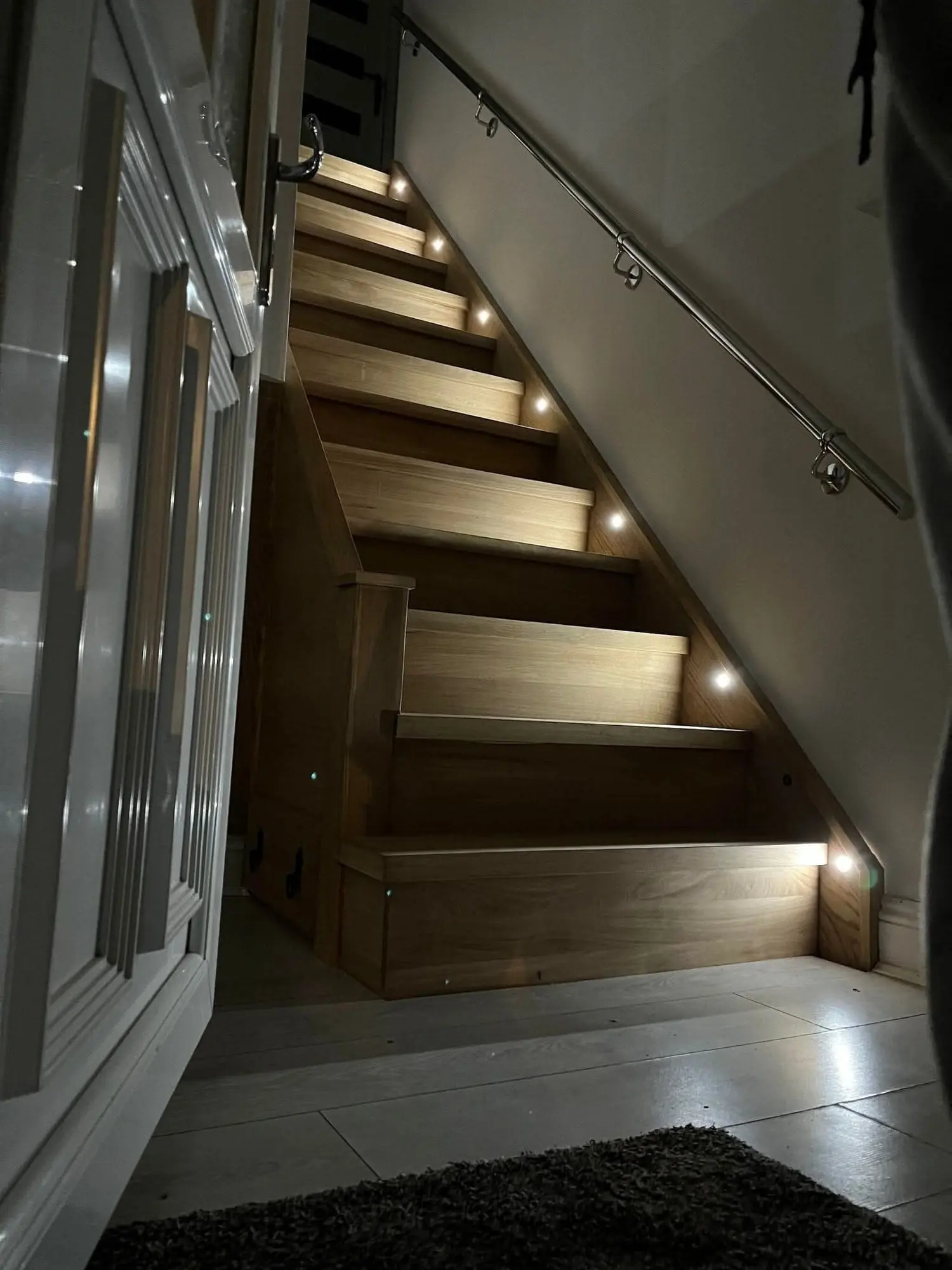 Oak staircase with step lights and a steel handrail beside a glazed door