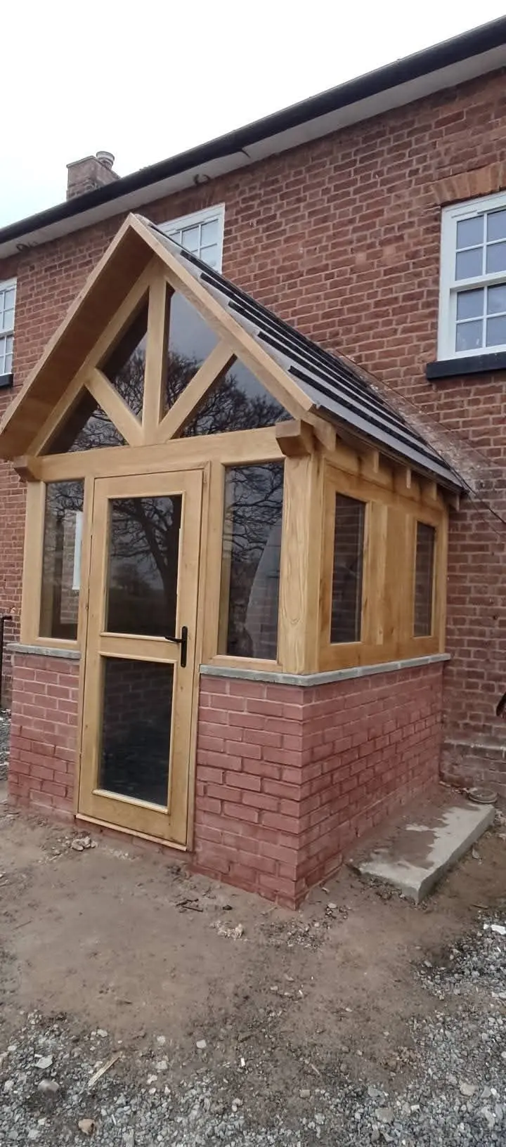 Oak-framed glazed porch with a pitched tiled roof on a red-brick house