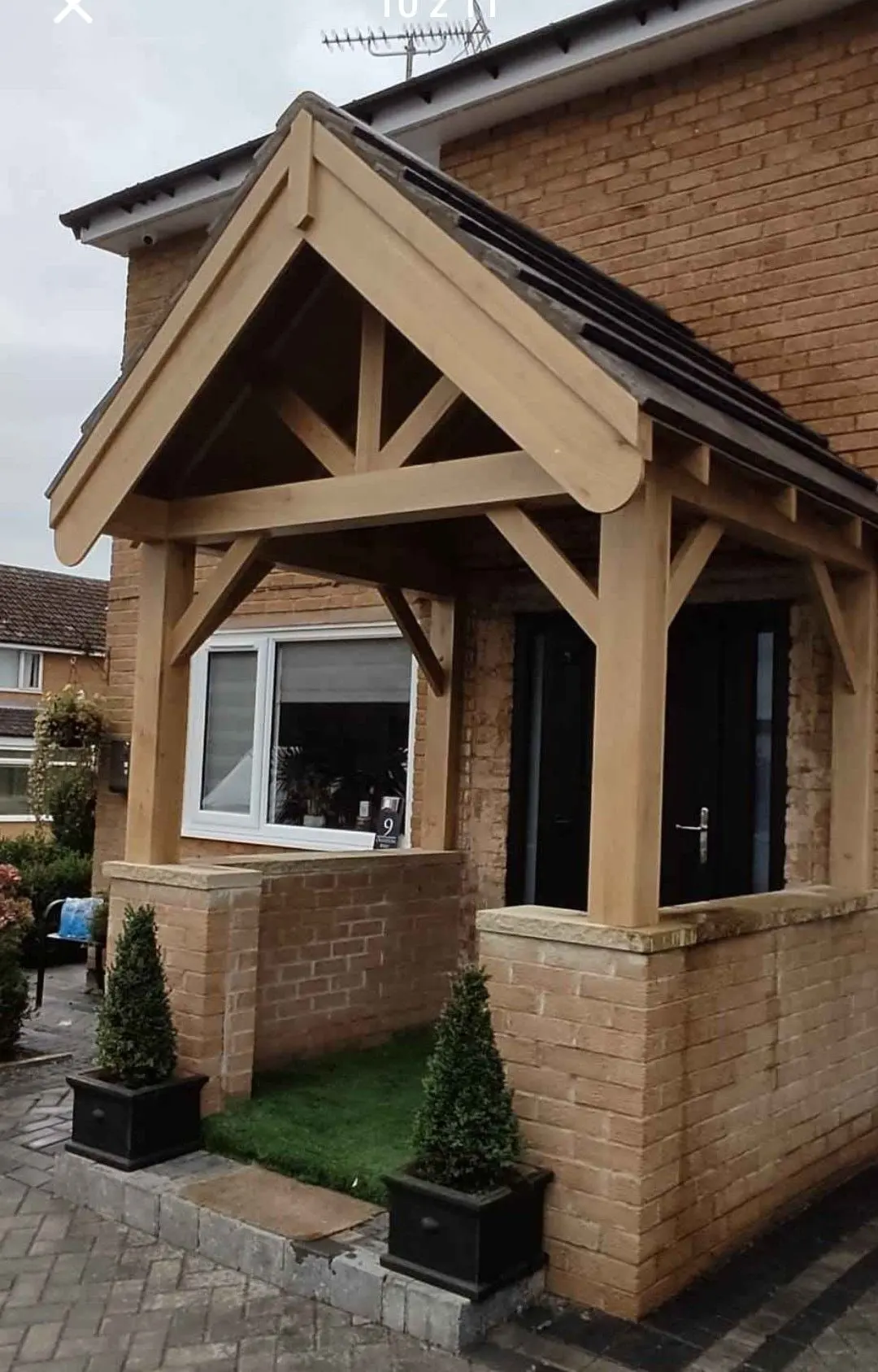 Large gabled oak porch on a brick house with planters either side of the door