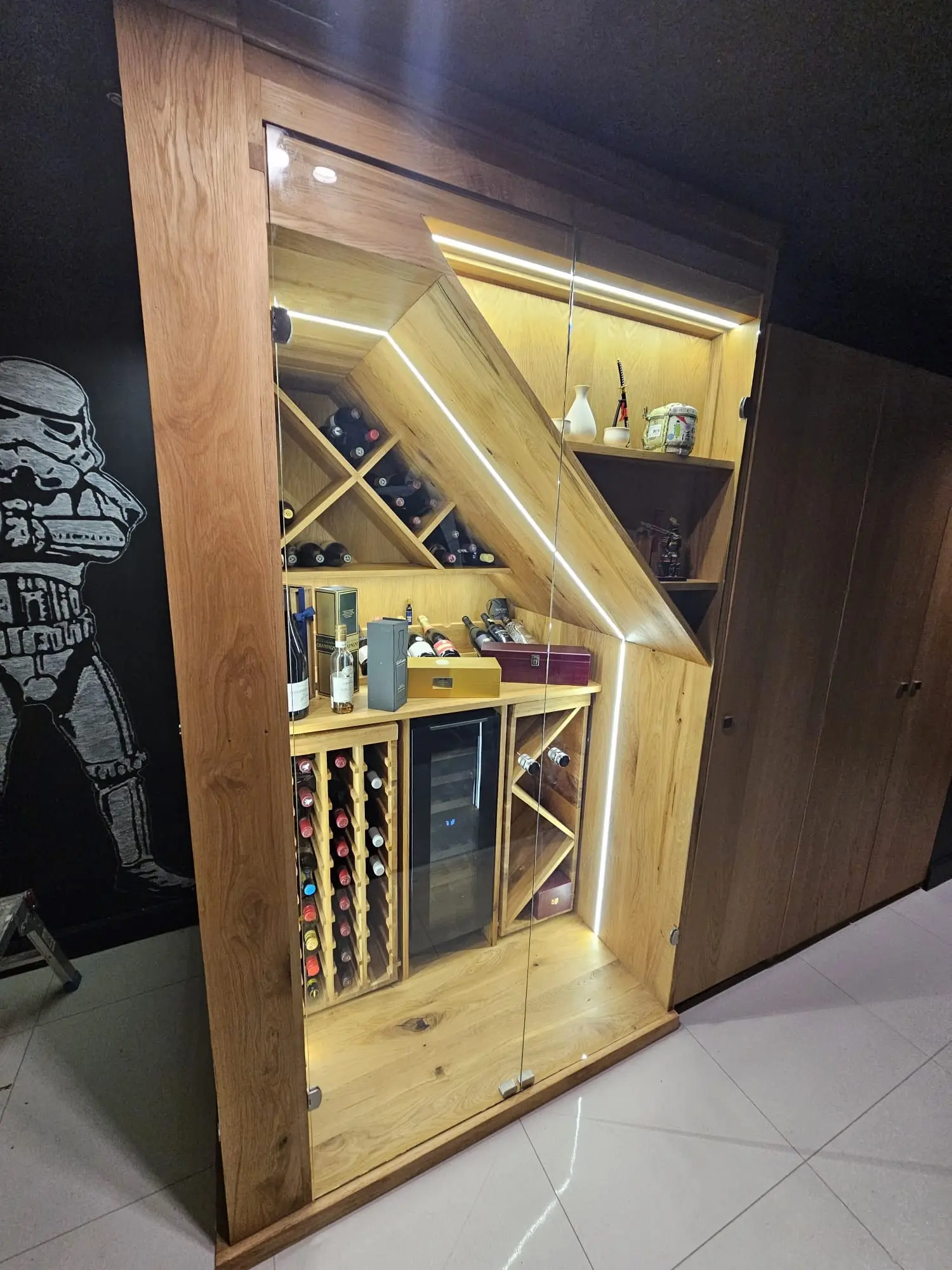 Solid oak wine cabinet built beneath a staircase, lit by LED strips behind a glass door